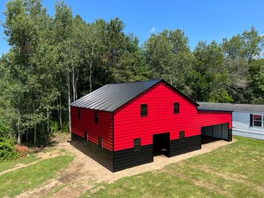 A red and black metal barn sits in a field.