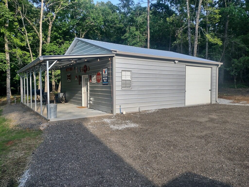 A gray metal building with a porch and a gravel driveway.